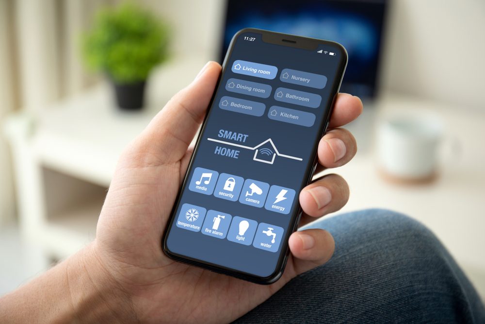 man hand holding phone with app smart home in room house