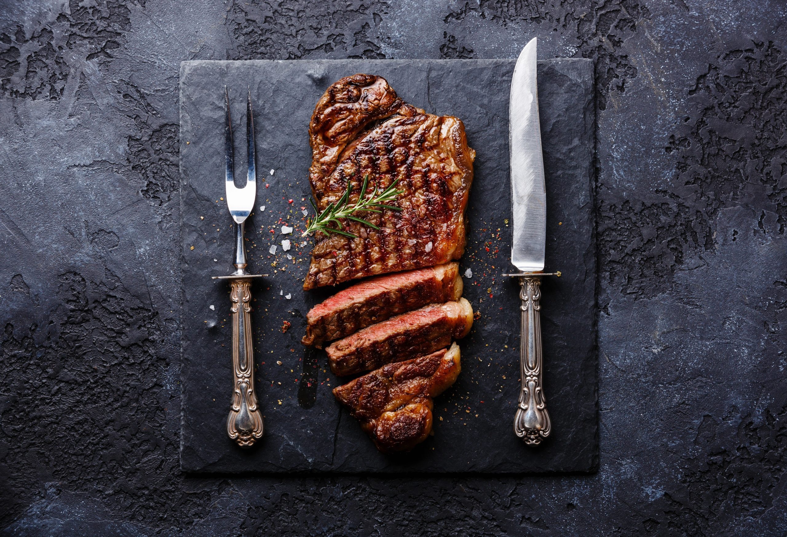 Sliced grilled meat barbecue steak Striploin with knife and fork carving set on black stone slate