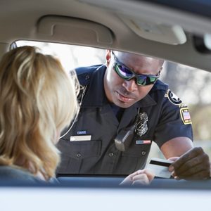 Police officer examines driver's license through car window in outdoor setting.