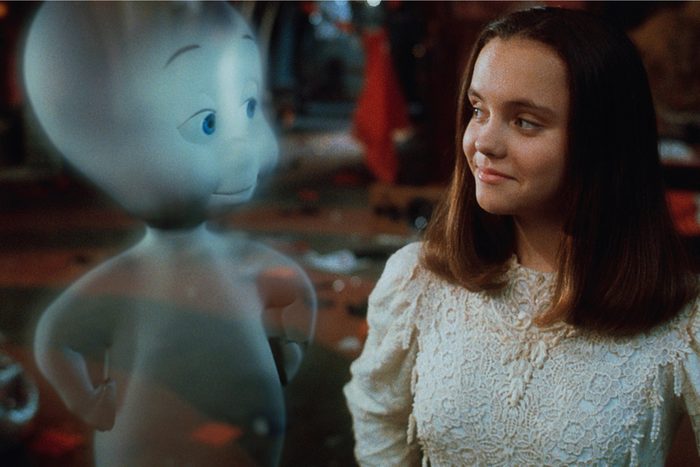 A friendly ghost converses with a smiling girl in a cluttered, warmly-lit room.