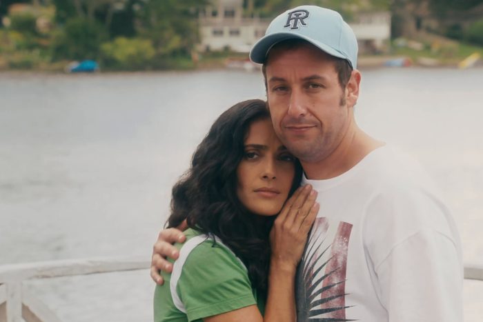 Two people embrace on a pier, surrounded by a tranquil lake and distant greenery, exuding a sense of warmth and connection.