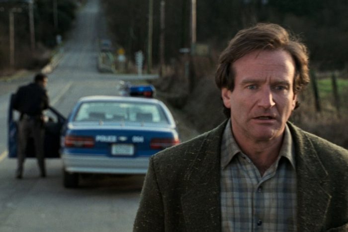 Man walking on a rural road, looking concerned. Police officer stands near an open car door in the background.