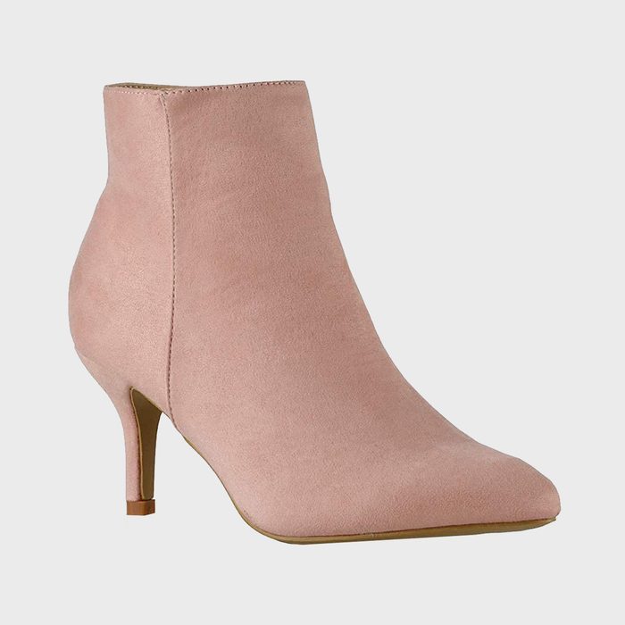 A pink suede ankle boot stands against a plain gray background, displaying a sleek design with a thin heel.