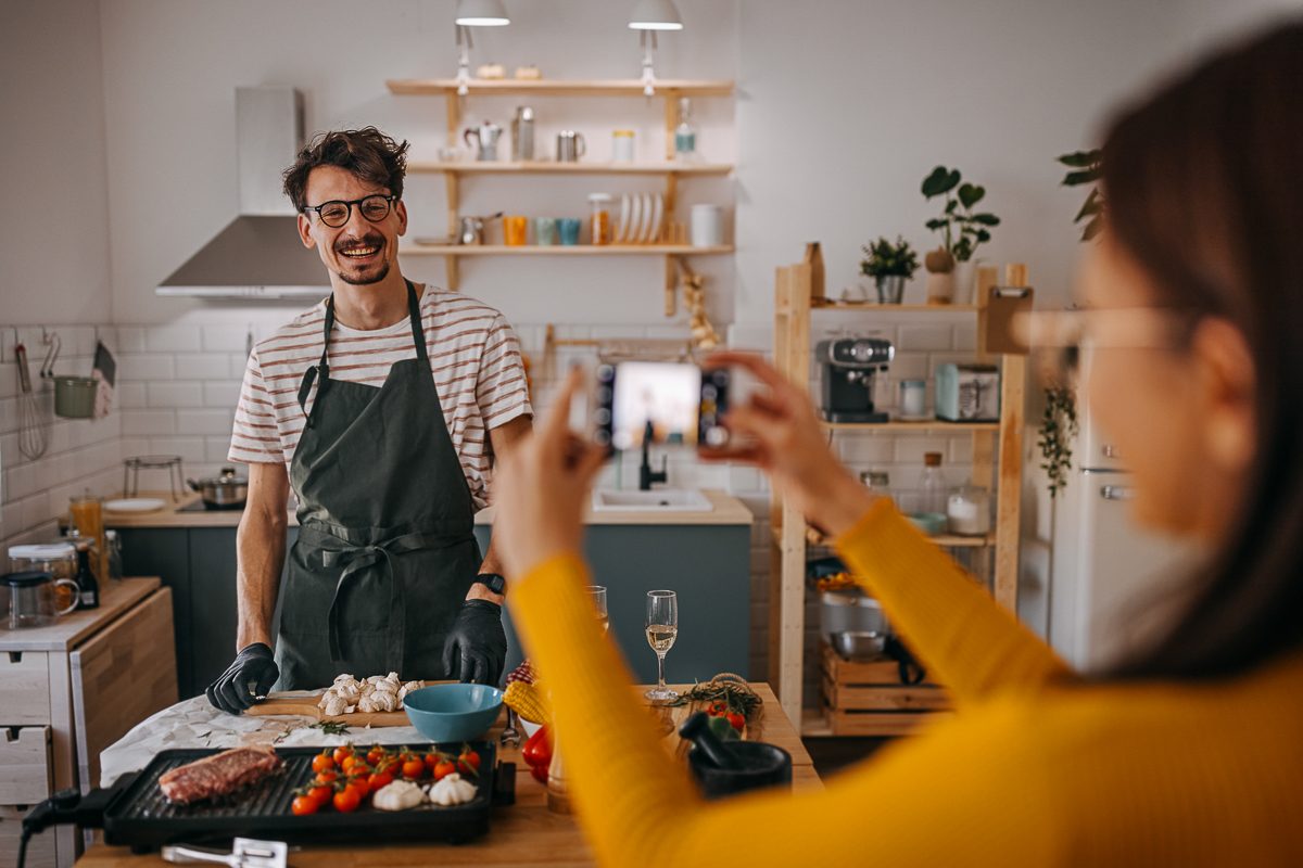 woman photographing man in kitchen