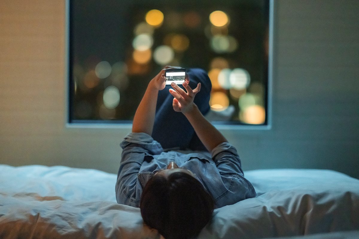 woman using phone lying on bed