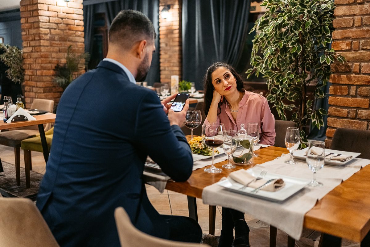 man using phone at dinner while woman is frustrated