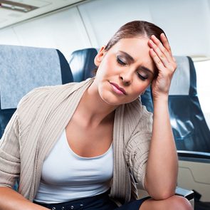 A young woman sitting on an airplane and suffering from headache.